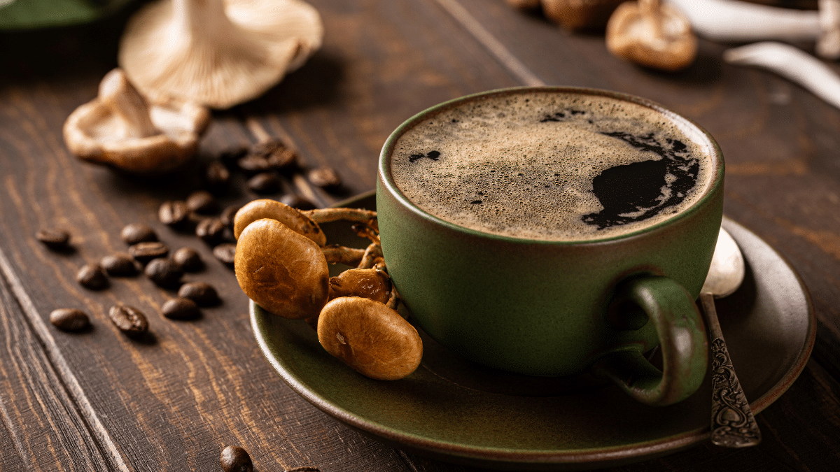 A cup of mushroom coffee surrounded by coffee beans and mushrooms